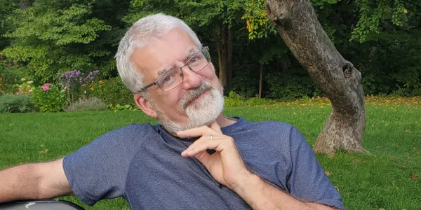 Founder of EAL, sitting on a bench in front of trees.